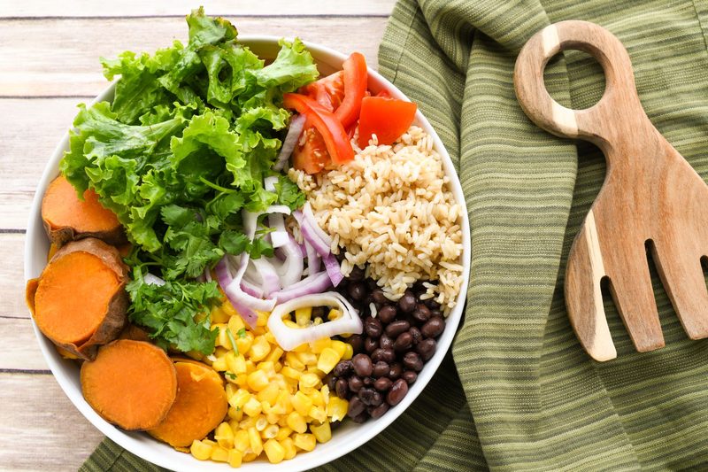 A colorful home-cooked meal of vegetables, beans and whole grains on a wooden table in natural light